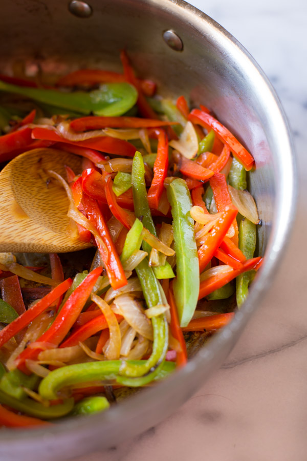 Caramelized onions, and some red and green bell peppers in a large skillet with a wooden spoon.
