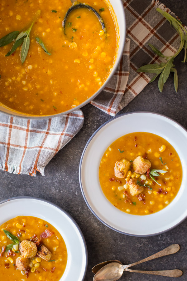 Two bowls of Butternut Squash Corn Chowder with Goat Cheese Croutons on top, sitting next to a large pot of Butternut Squash Corn Chowder.