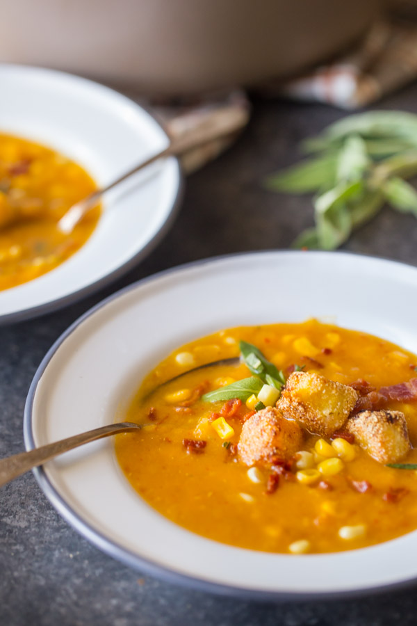 A bowl of Butternut Squash Corn Chowder with Goat Cheese Croutons on top, and other bowl of chowder in the background. 