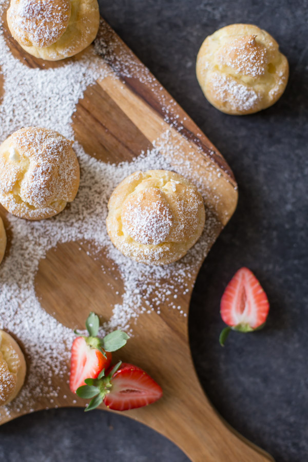 Classic Cream Puffs dusted with powdered sugar, sitting on a cutting board.