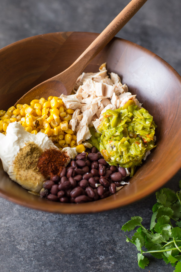 All the ingredients for the filling of the Hatch Green Chile Chicken Enchiladas in a large wood bowl with a wooden spoon in it.