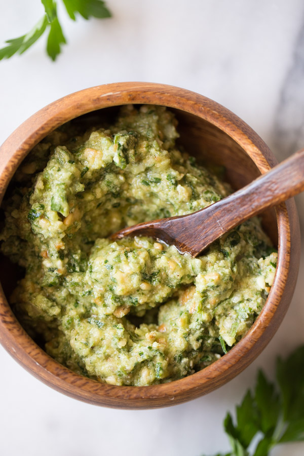 A small wood bowl of Pesto with a little wood spoon in it.