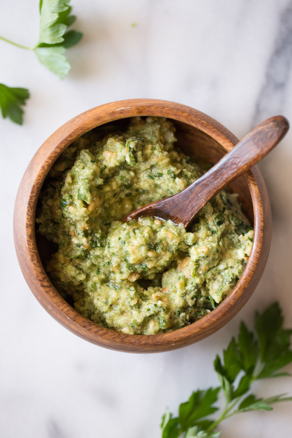 A small wood bowl of Pesto with a little wood spoon in it.