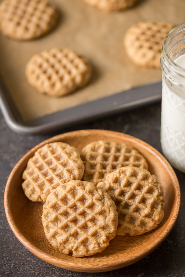 Small Batch Peanut Butter Cookies on a wood plate, sitting next to a glass of milk and a baking sheet of cookies in the background. 
