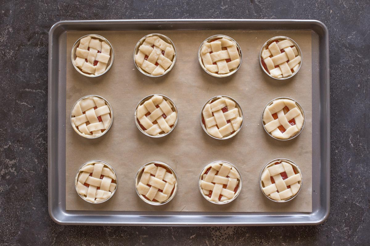 Mini Mason Jar Lid Strawberry Pies assembled and arranged on a parchment paper lined baking sheet before baking.