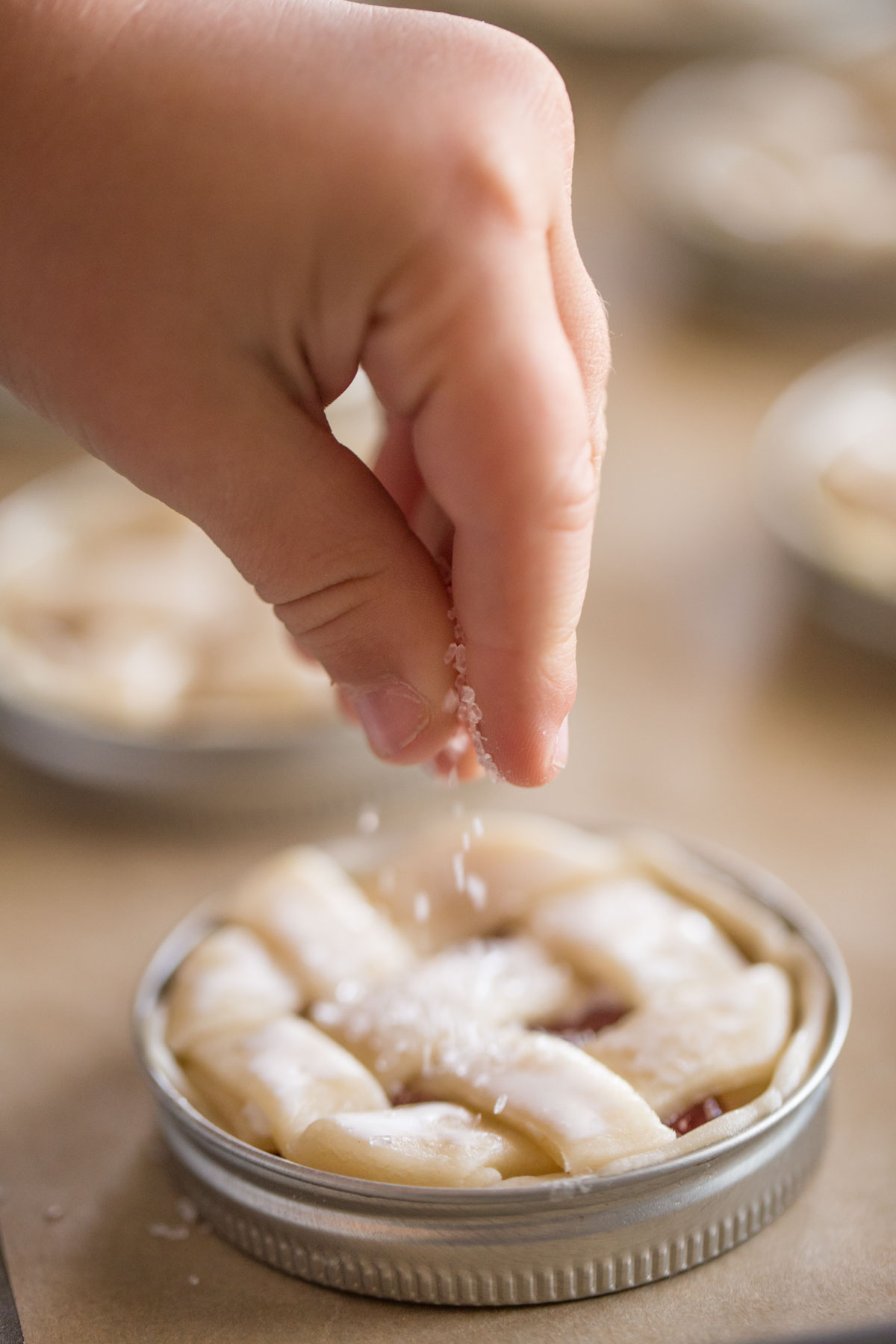 Sparkling sugar being sprinkled on top of a Mason Jar Lid Strawberry Pie.