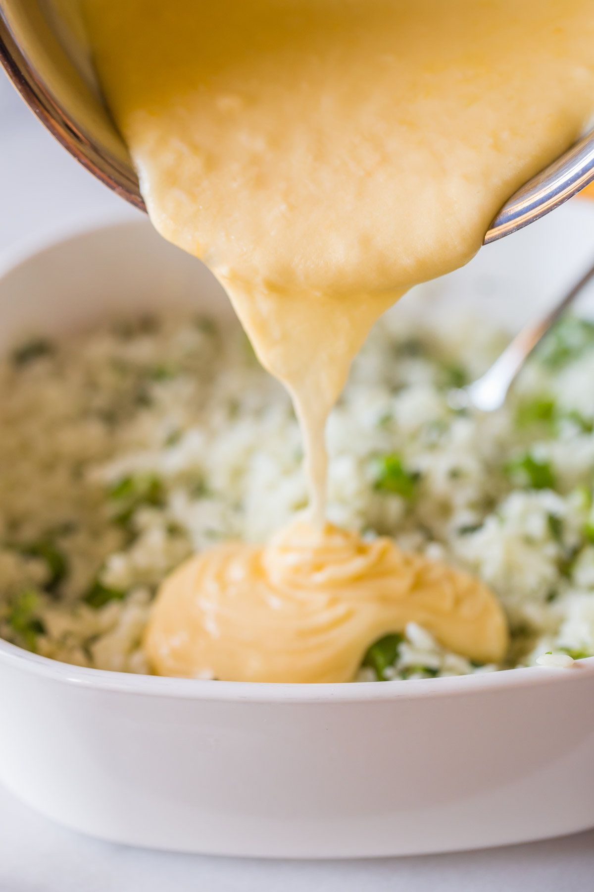 The creamy cheddar cheese sauce being poured on top of the baking dish of white rice and broccoli for the Cheesy Broccoli Rice.