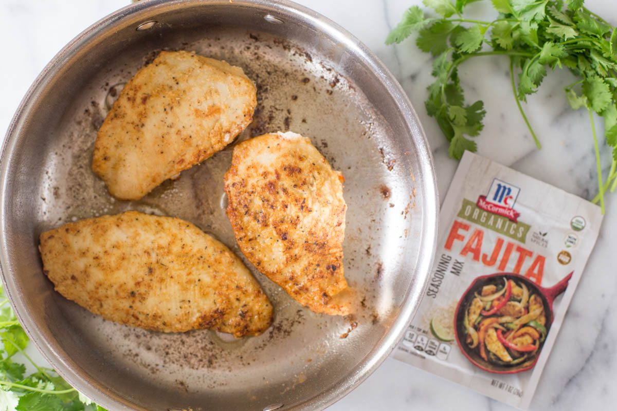 A skillet with the cooked chicken in it, with a packet of the McCormick Organics Fajita Seasoning Mix next to it.
