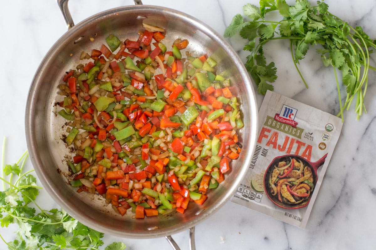 A skillet with the cooked red and green peppers and onions in it, with a packet of the McCormick Organics Fajita Seasoning Mix next to it.