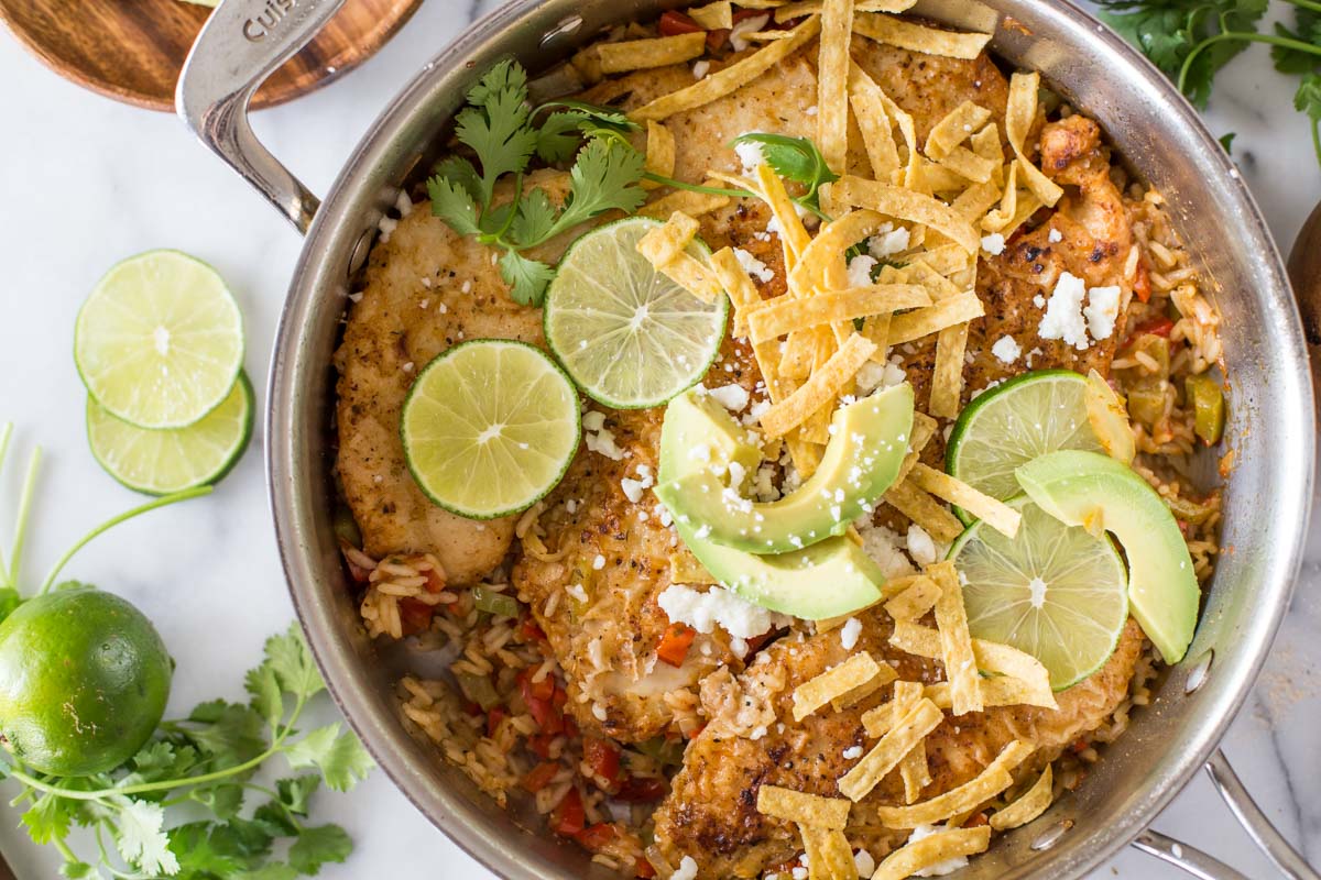 One Skillet Fajita Style Chicken and Rice, topped with crumbled queso fresco, fresh cilantro, tortilla strips, sliced avocado, and lime slices.