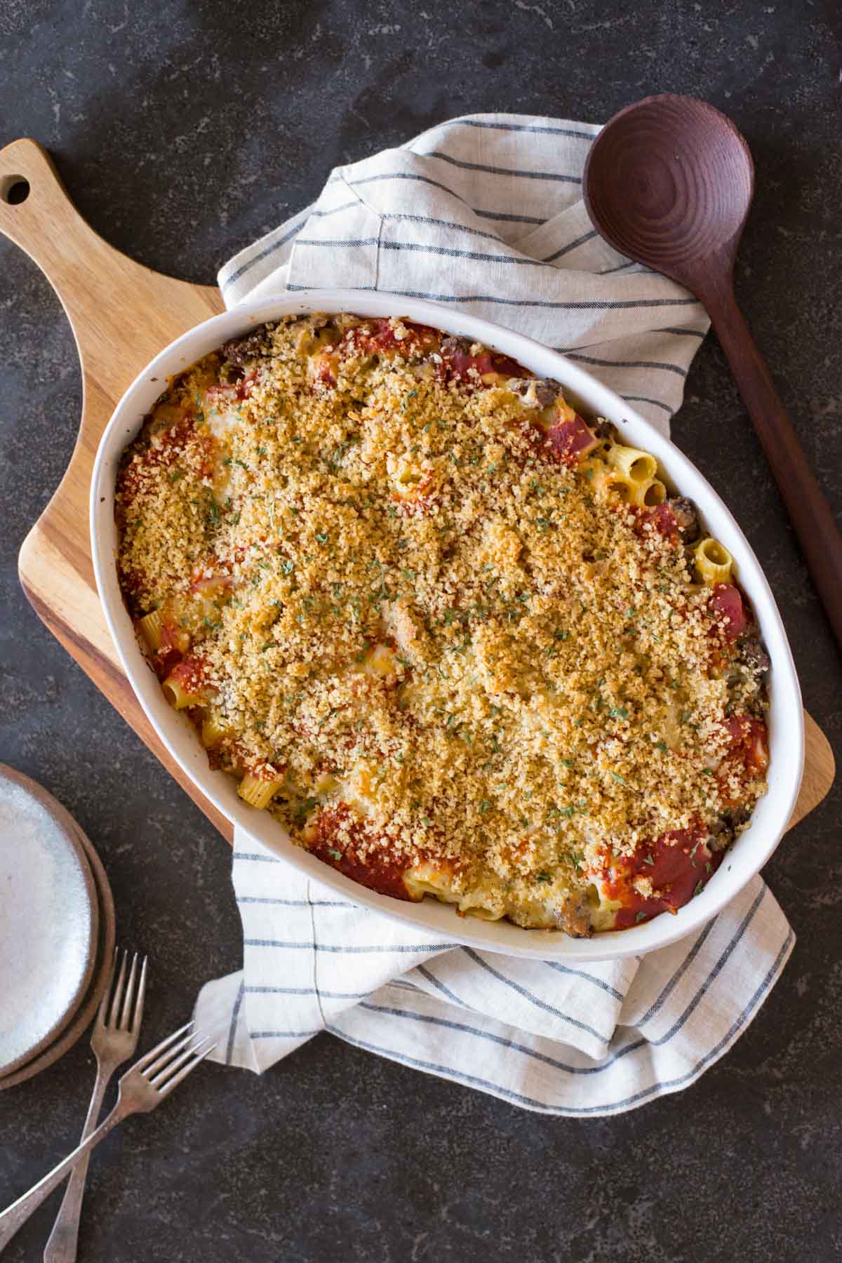 Cheesy Tomato Alfredo Pasta Bake in a baking dish, with a serving spoon, plates and forks beside it.