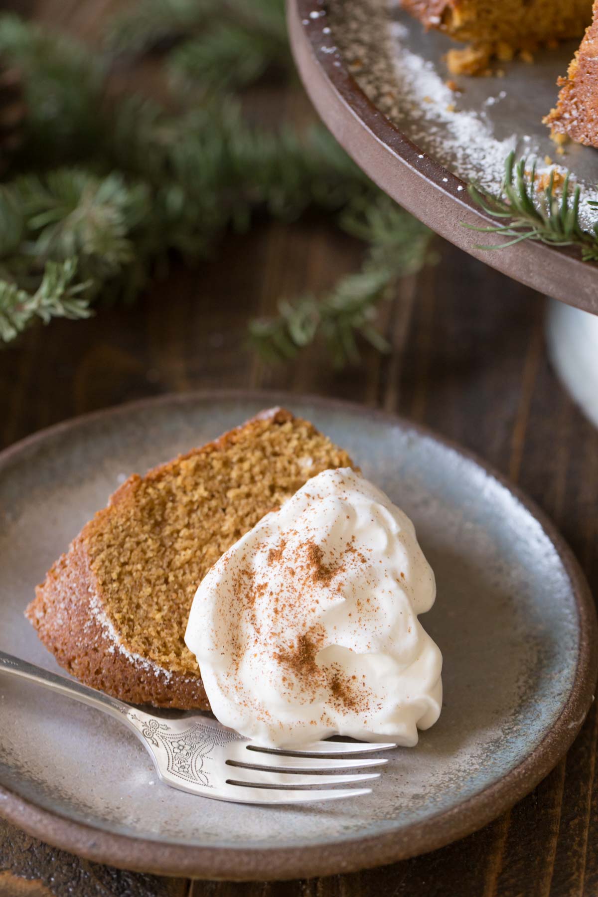 A slice of Gingerbread Bundt Cake topped with whipped cream, on a plate with a fork.