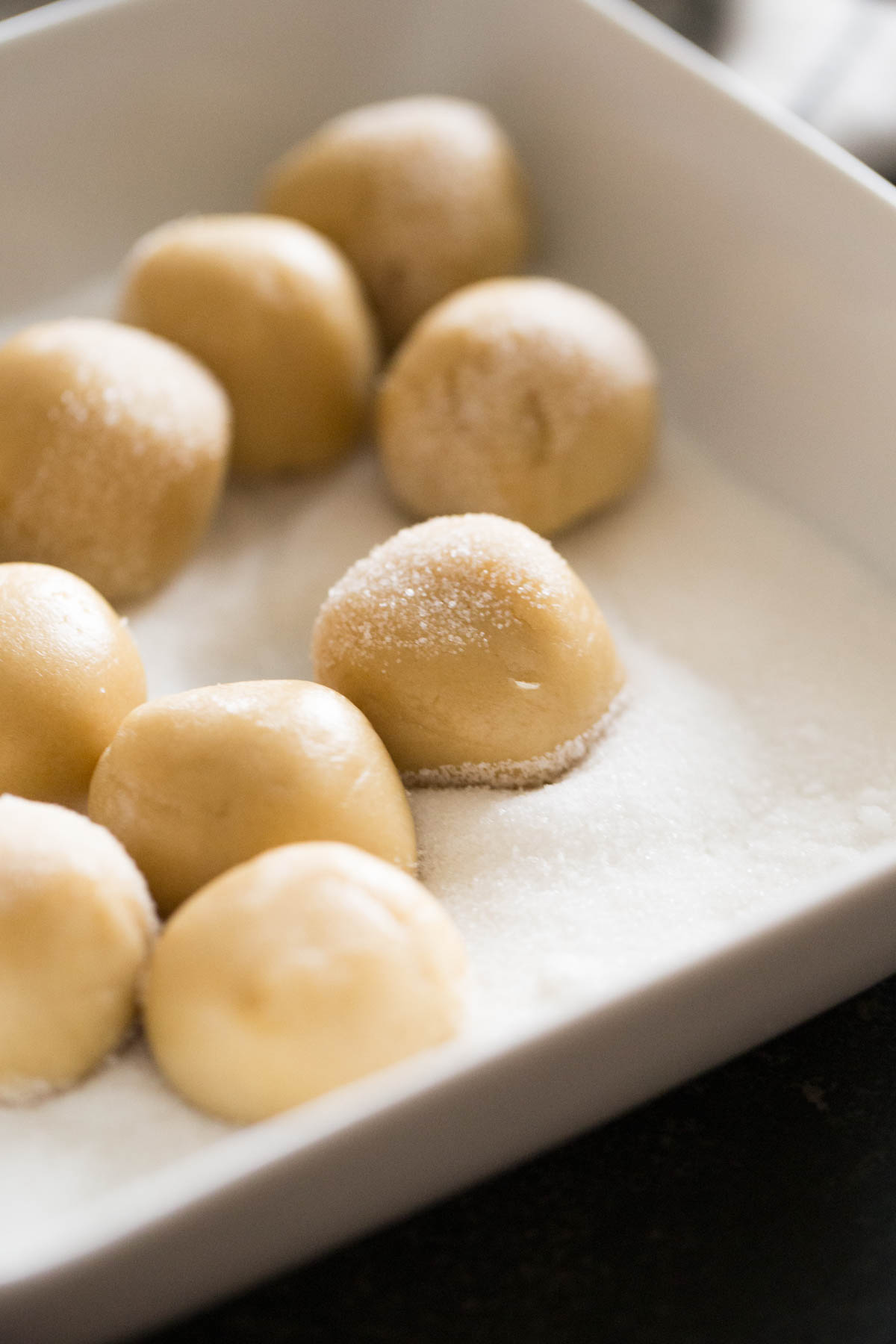 Brown Butter Almond Crinkle Cookie dough balls in a bowl of granulated sugar. 