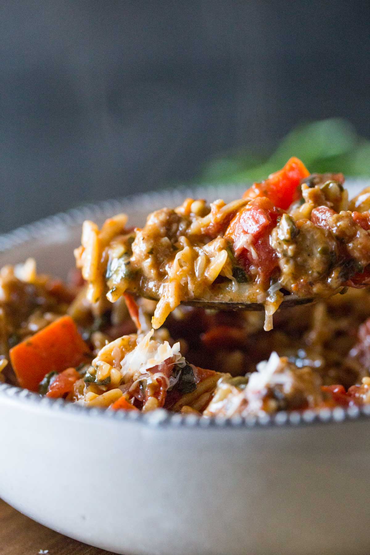 A spoon full of One Pot Creamy Tomato Orzo held over the bowl.