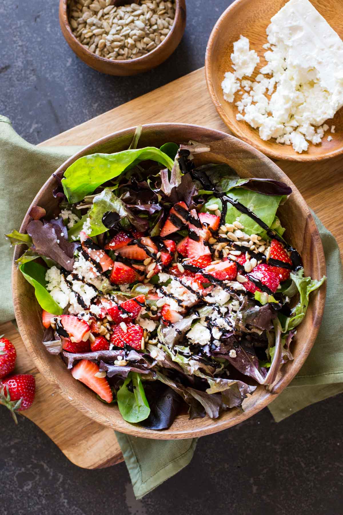A bowl of Easy Strawberry Balsamic Salad sitting next to a small bowl of crumbled feta and a small bowl of sunflower seeds. 