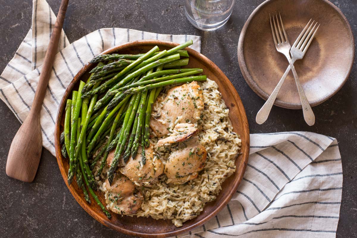 One Pot Chicken and Rice Dinner on a large serving plate, sitting next to some plates, forks, a glass and a wooden spoon.  