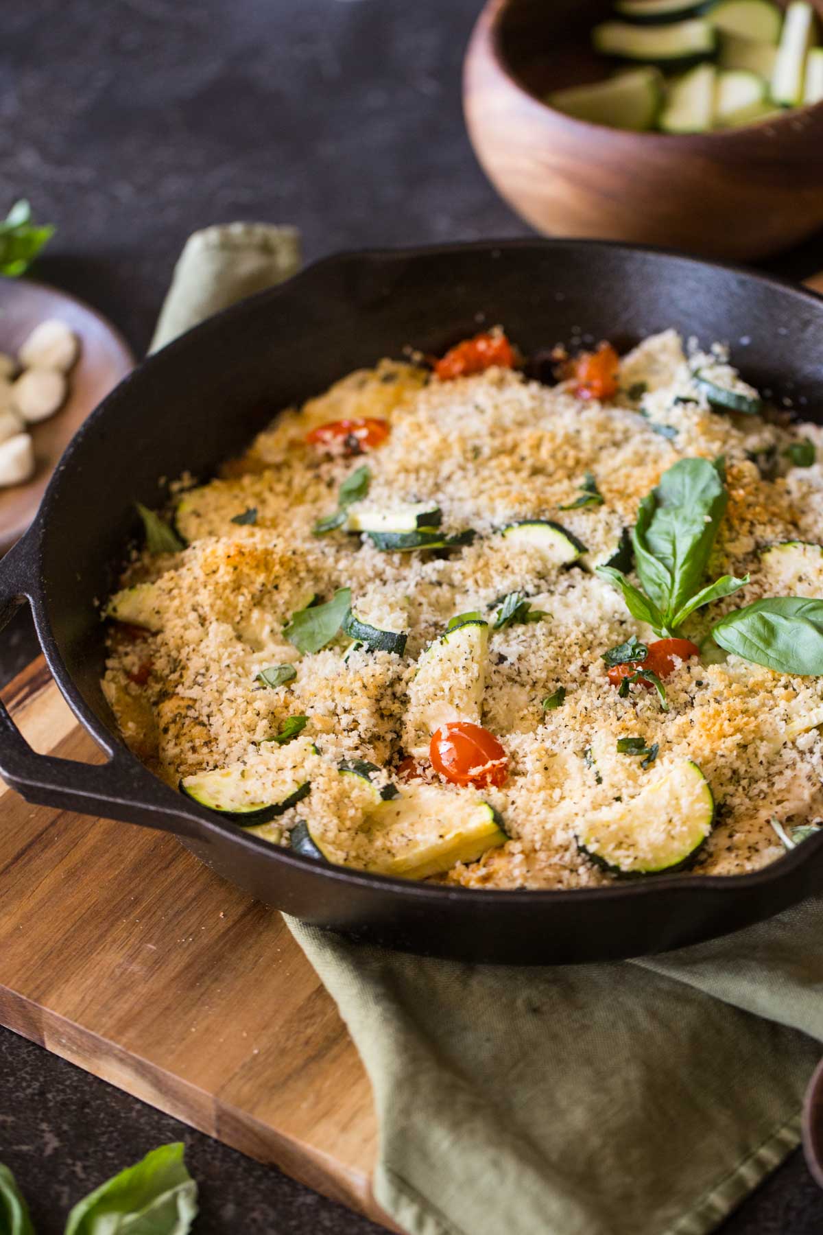 Pesto Chicken Skillet garnished with fresh basil, with a bowl of zucchini slices in the background.