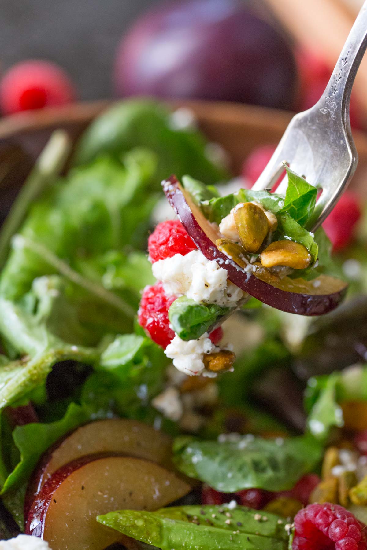 A fork full of Summer Fruited Salad with Goat Cheese and Pistachios held over the bowl of salad. 