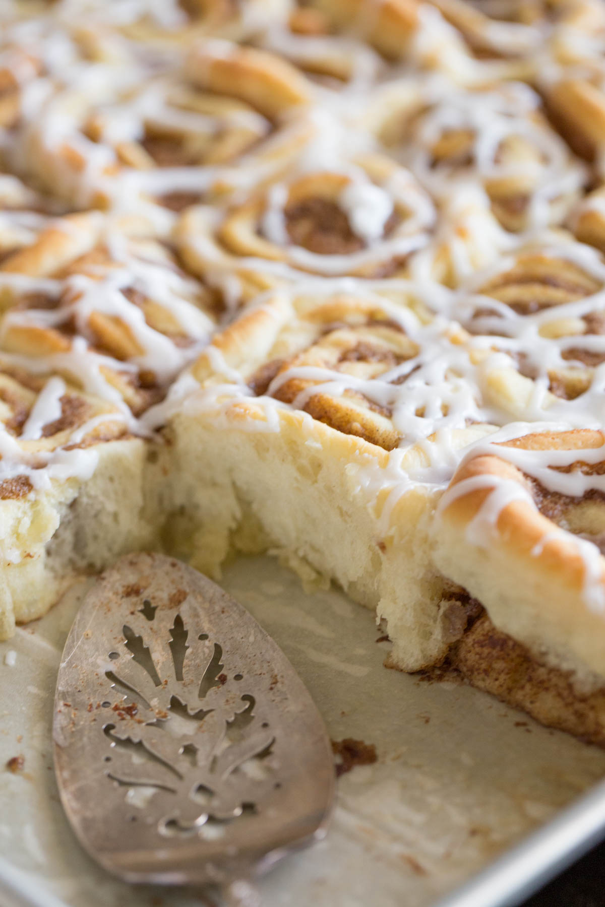 Sheet Pan Cinnamon Rolls in the baking sheet with a serving utensil and some of the rolls missing.