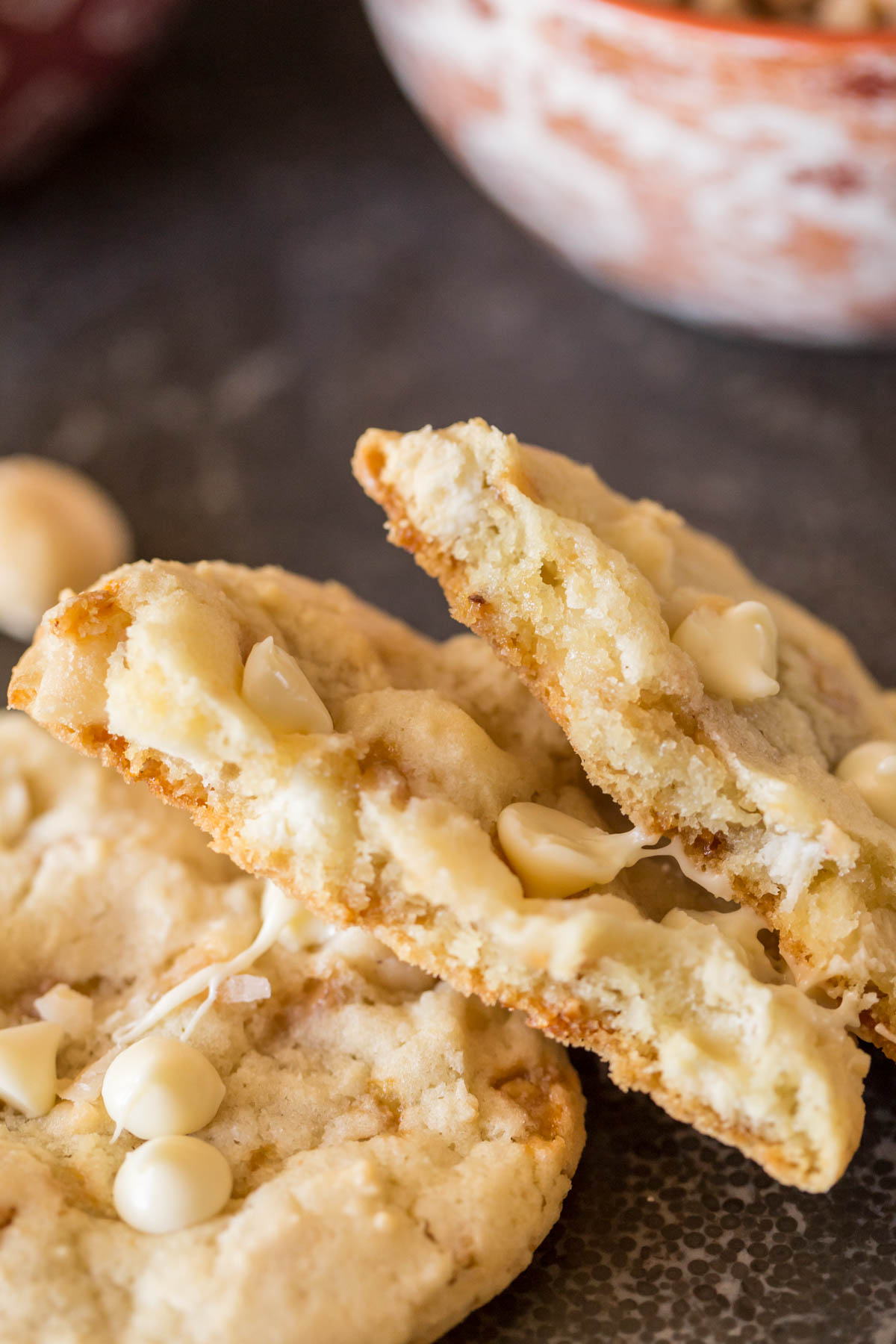 A Buttery Toffee White Chocolate Chip Macadamia Nut Cookie broken in half and stacked on top of a whole cookie. 