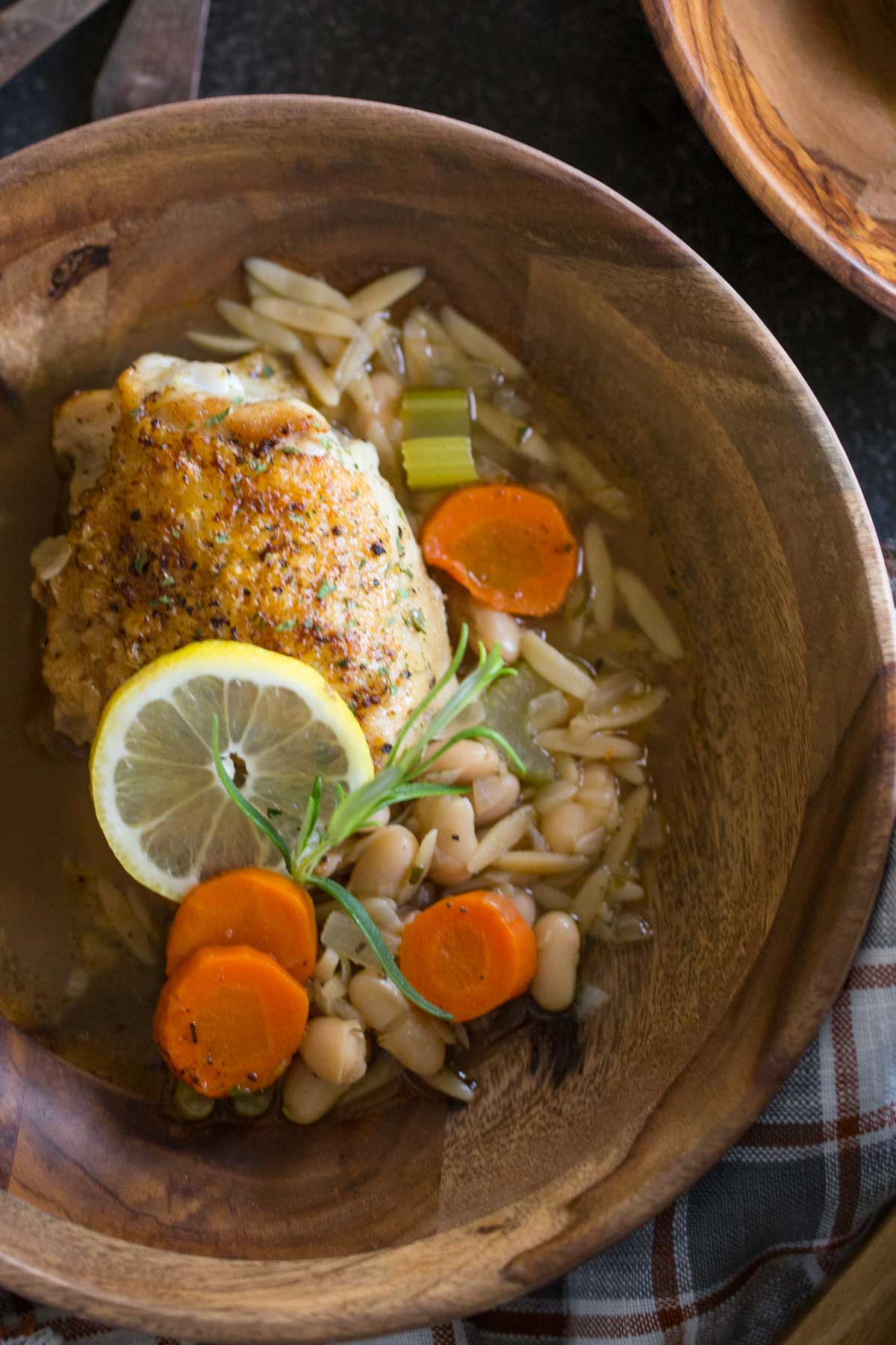 Rustic Lemon Rosemary Chicken and Orzo in a wood bowl, garnished with rosemary and a lemon slice.  