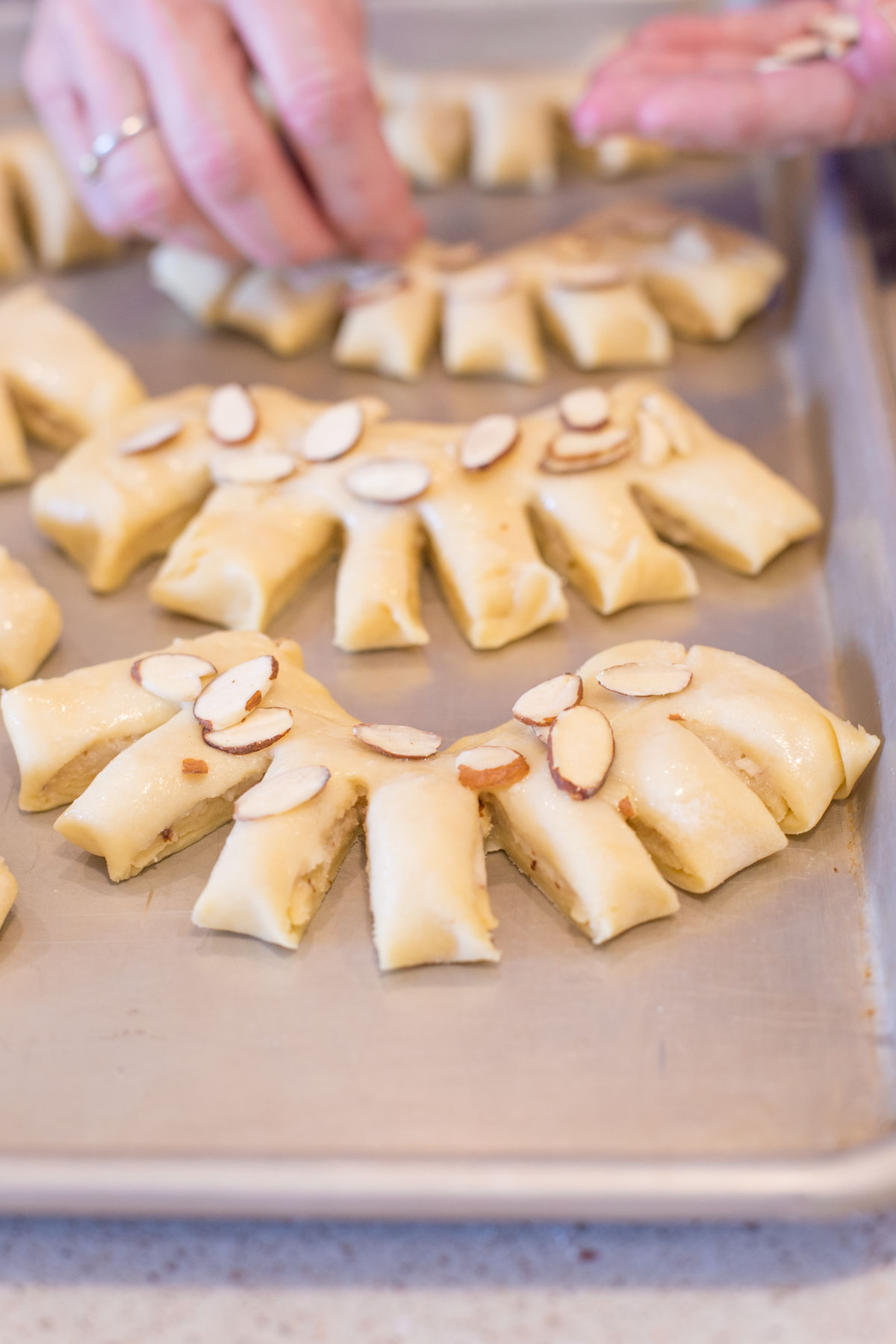 Sliced almonds being placed on top of the Buttery Almond Bear Claws on a baking sheet prior to baking.