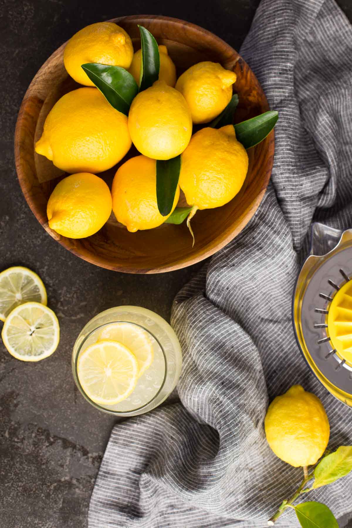 Top down view of wooden bowl of lemons with a glass of lemonade and lemon slices.