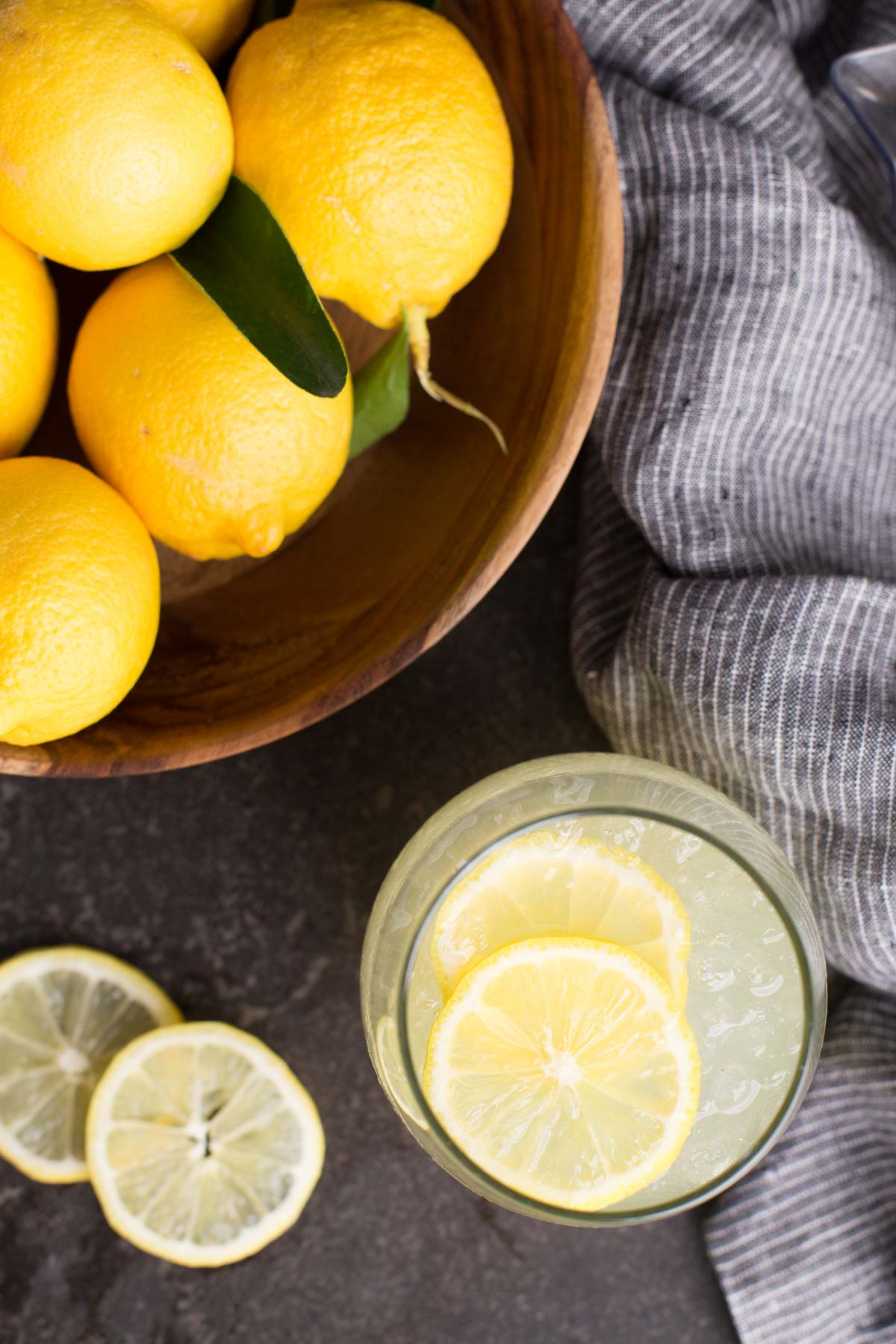 Wooden bowl of freshly picked lemons and a glass of lemonade poured.