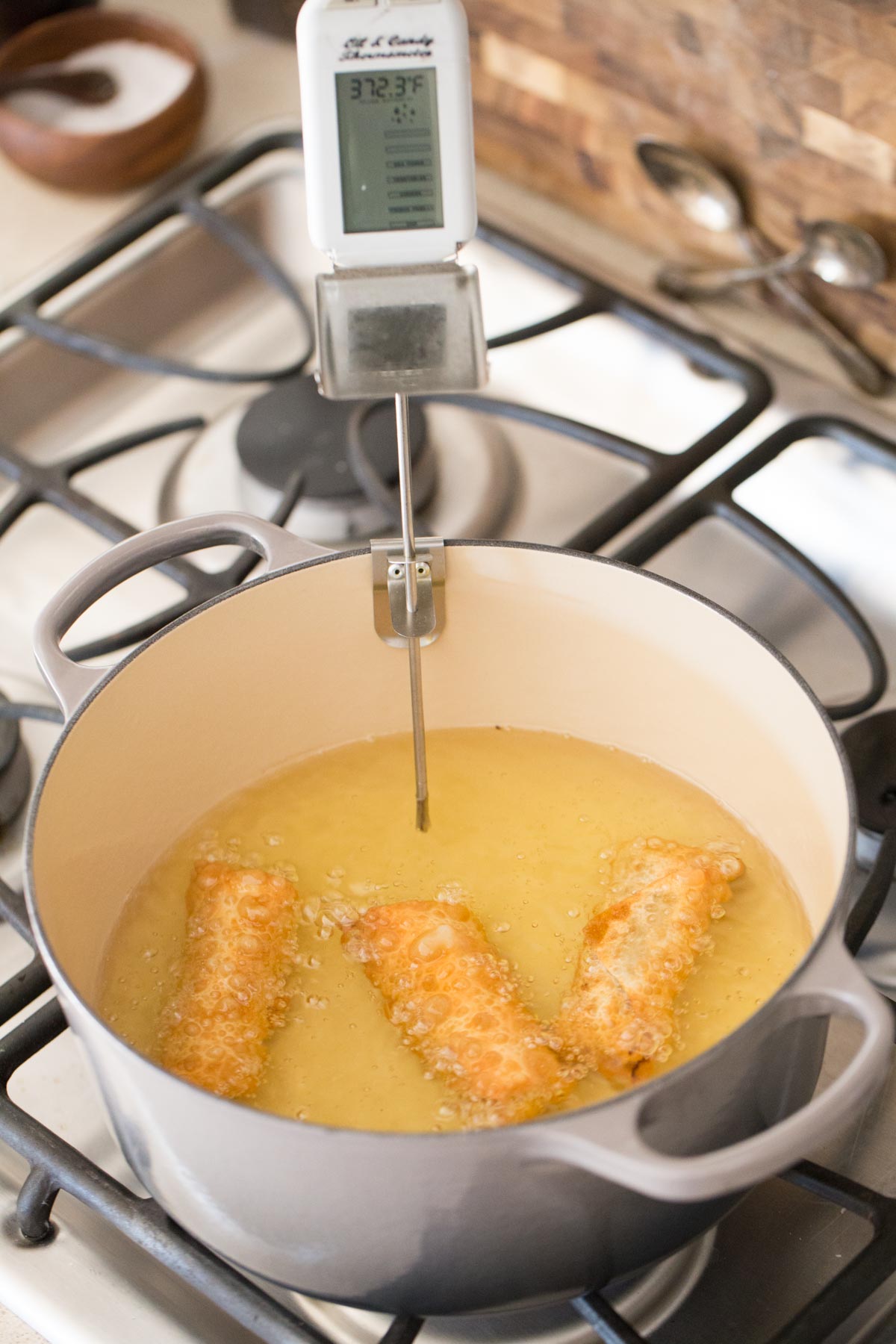 Three Fried Sloppy Joe Rolls in a heavy bottomed pot of oil with a thermometer in it. 