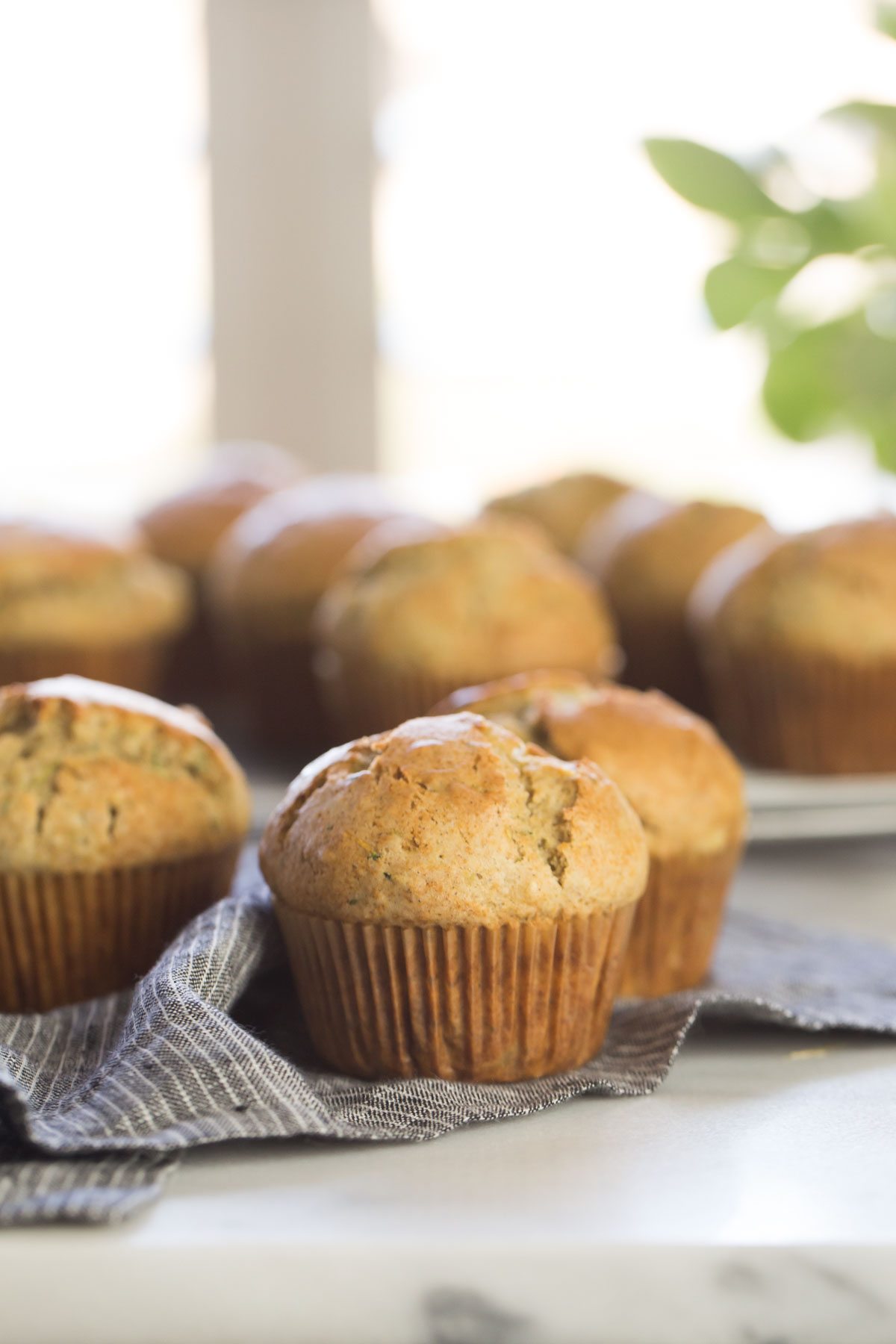 Three Healthier Zucchini Muffins on a cloth napkin, with more muffins in the background.
