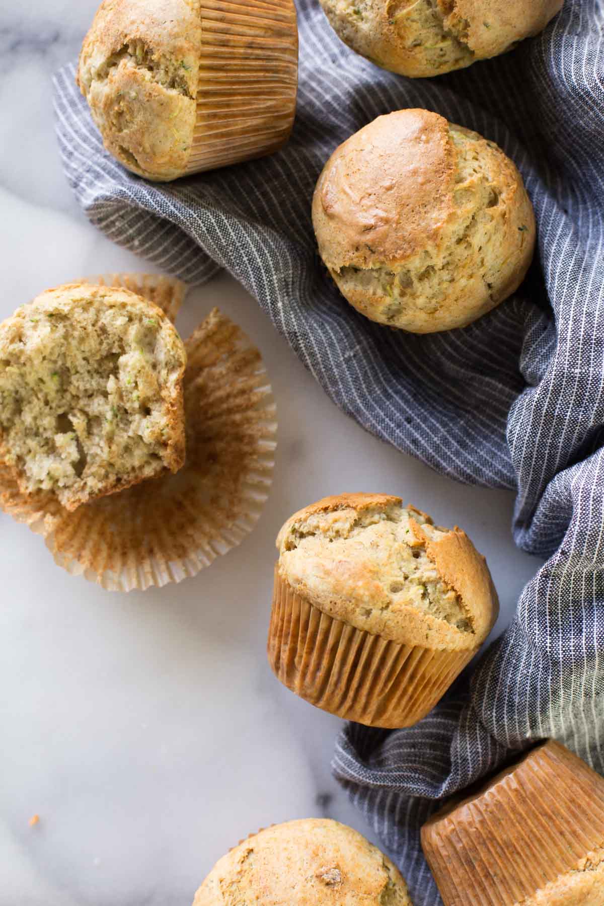 A half of a Healthier Zucchini Muffin sitting on its wrapper, with more whole muffins around it.