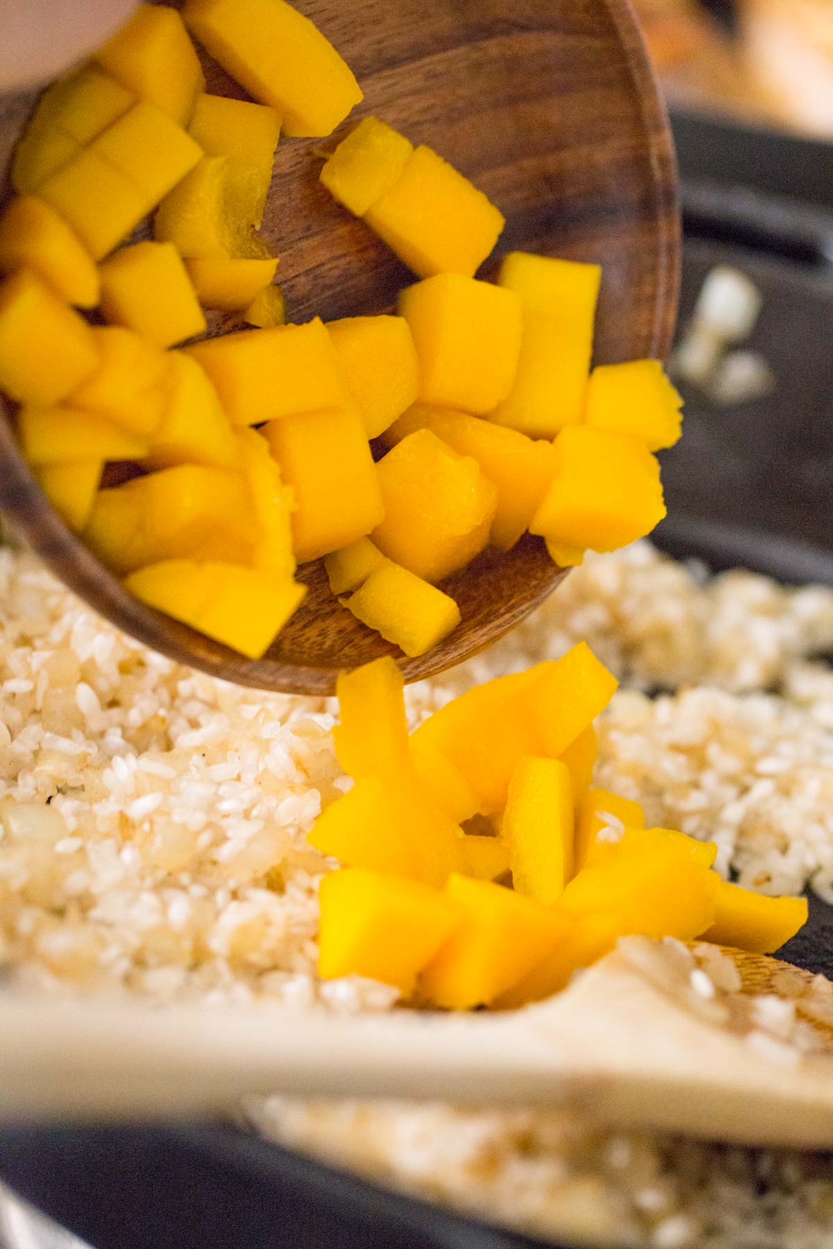 The cut mango being poured into the skillet with the rice mixture for the Chili Lime Mango Chicken and Rice. 