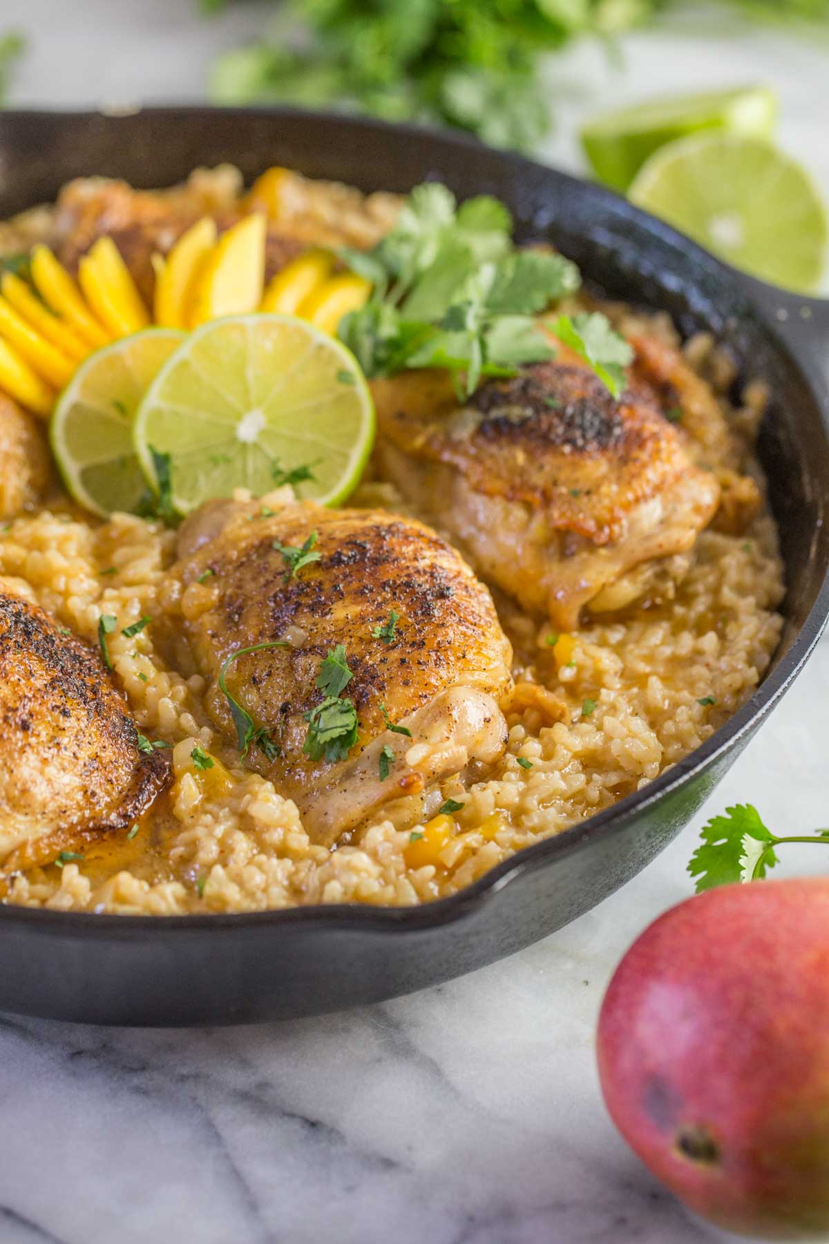 Chili Lime Mango Chicken and Rice in a cast iron skillet, garnished with fresh cilantro, mango and lime slices.