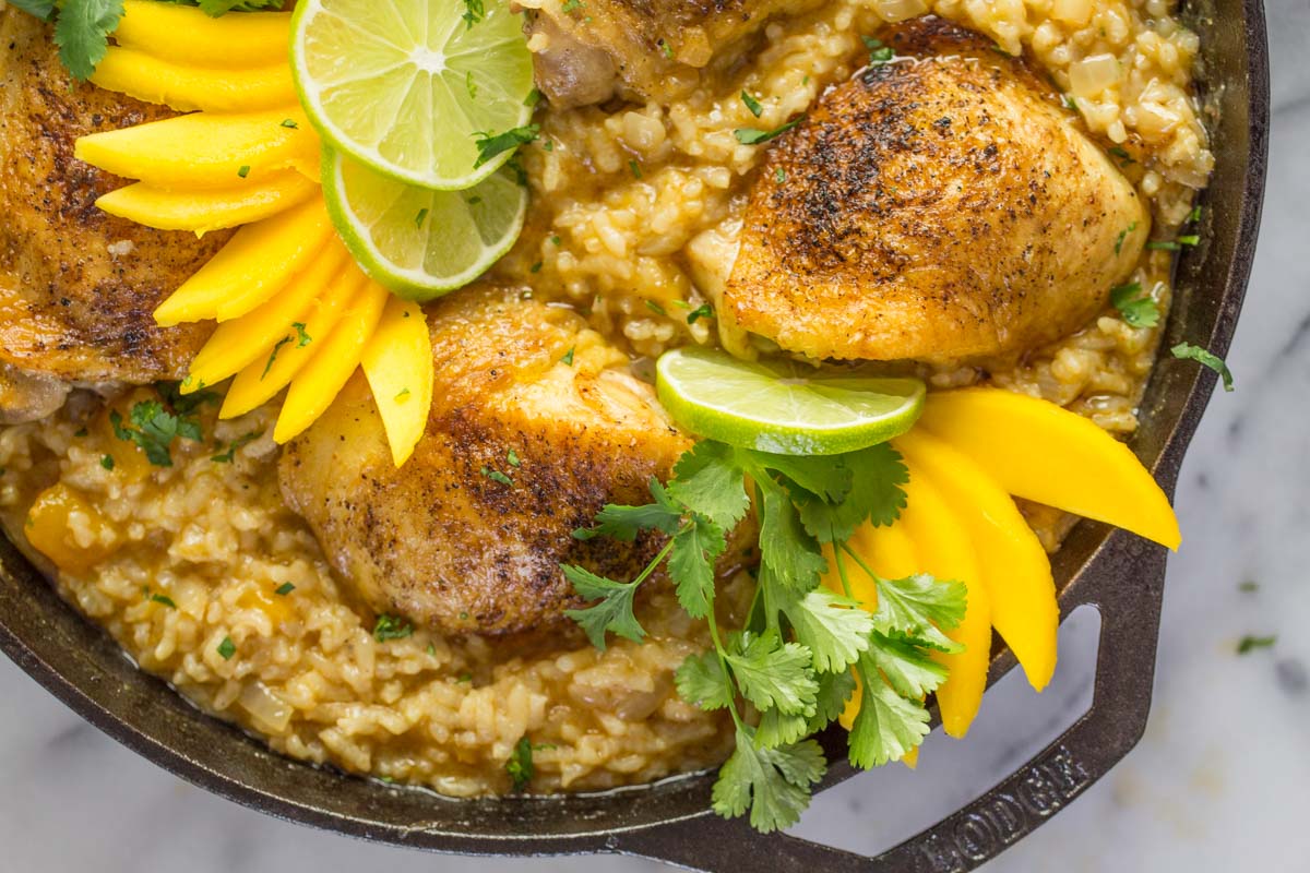 Chili Lime Mango Chicken and Rice in a cast iron skillet, garnished with fresh cilantro, mango and lime slices.
