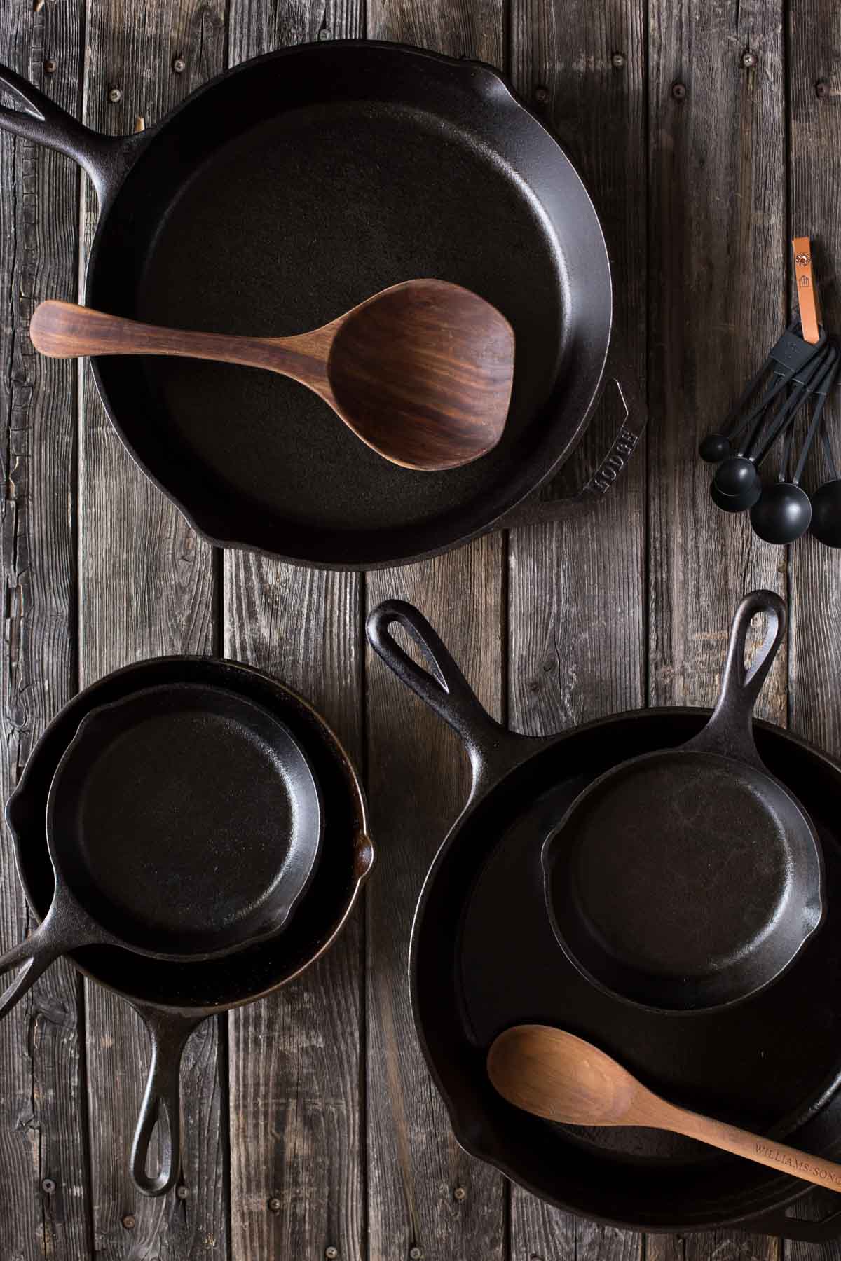 Various sizes of cast iron skillets on a wooden board.