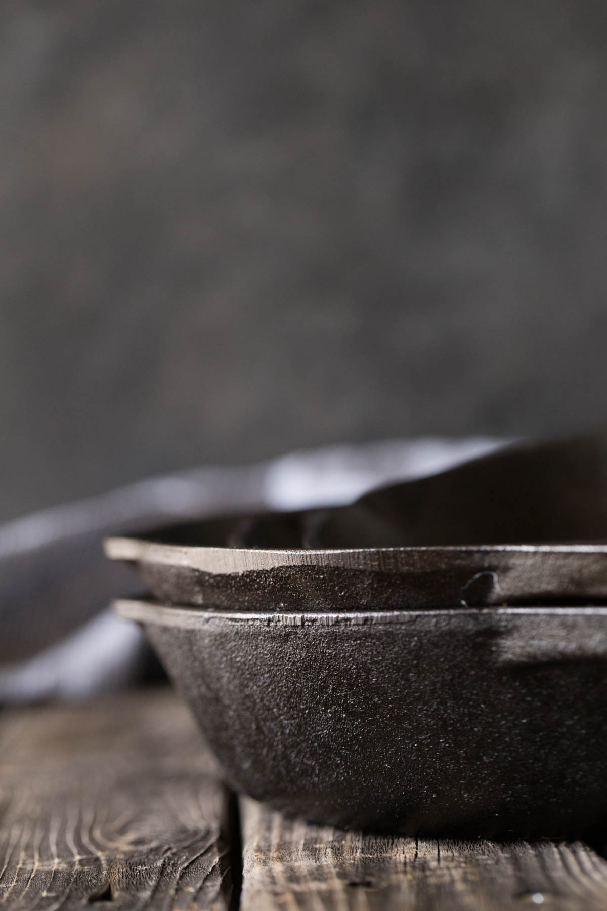 A close up view of cast iron skillets from the side with a grey background. 