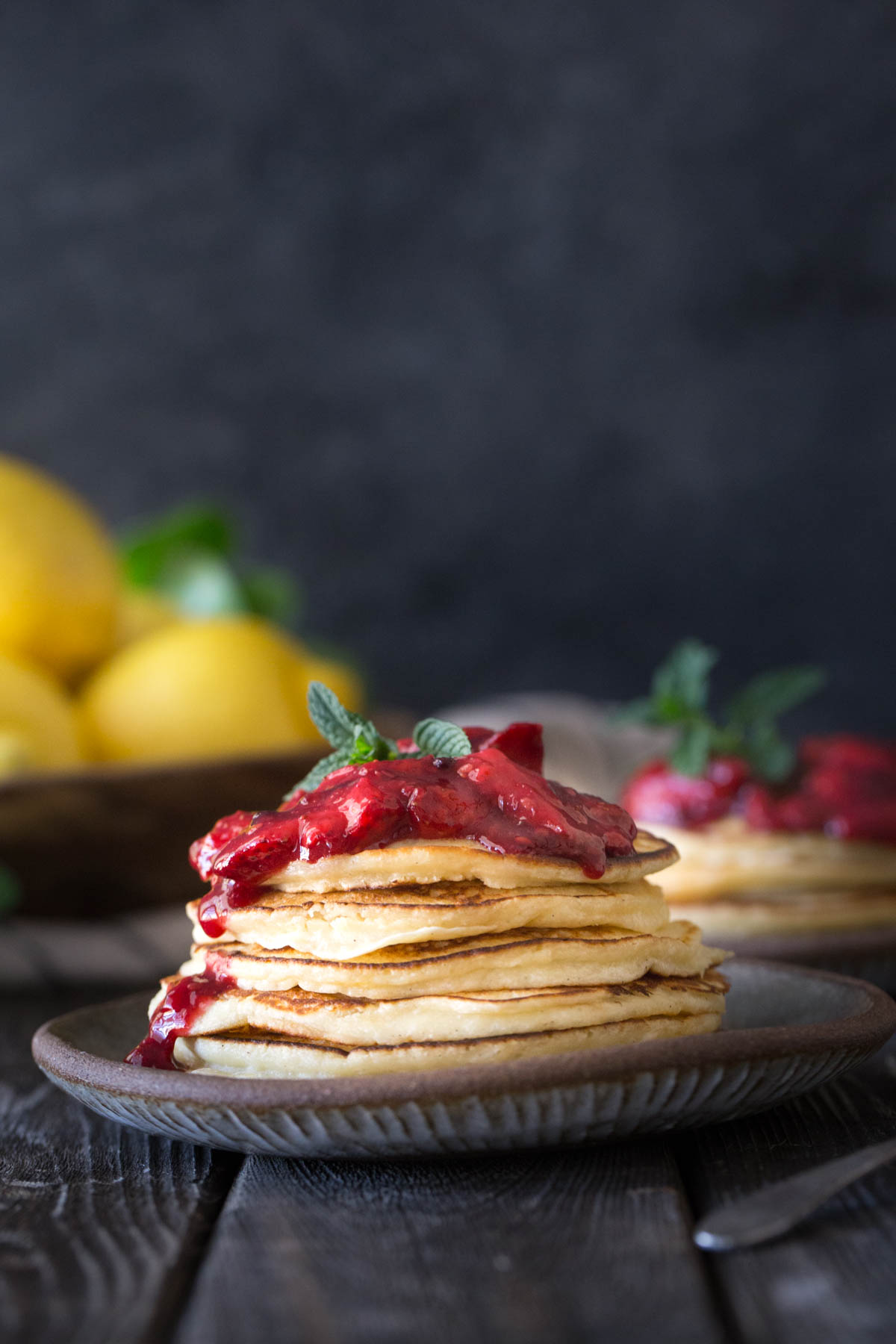 A stack of Lemon Ricotta pancakes with fresh berry sauce on a grey background.