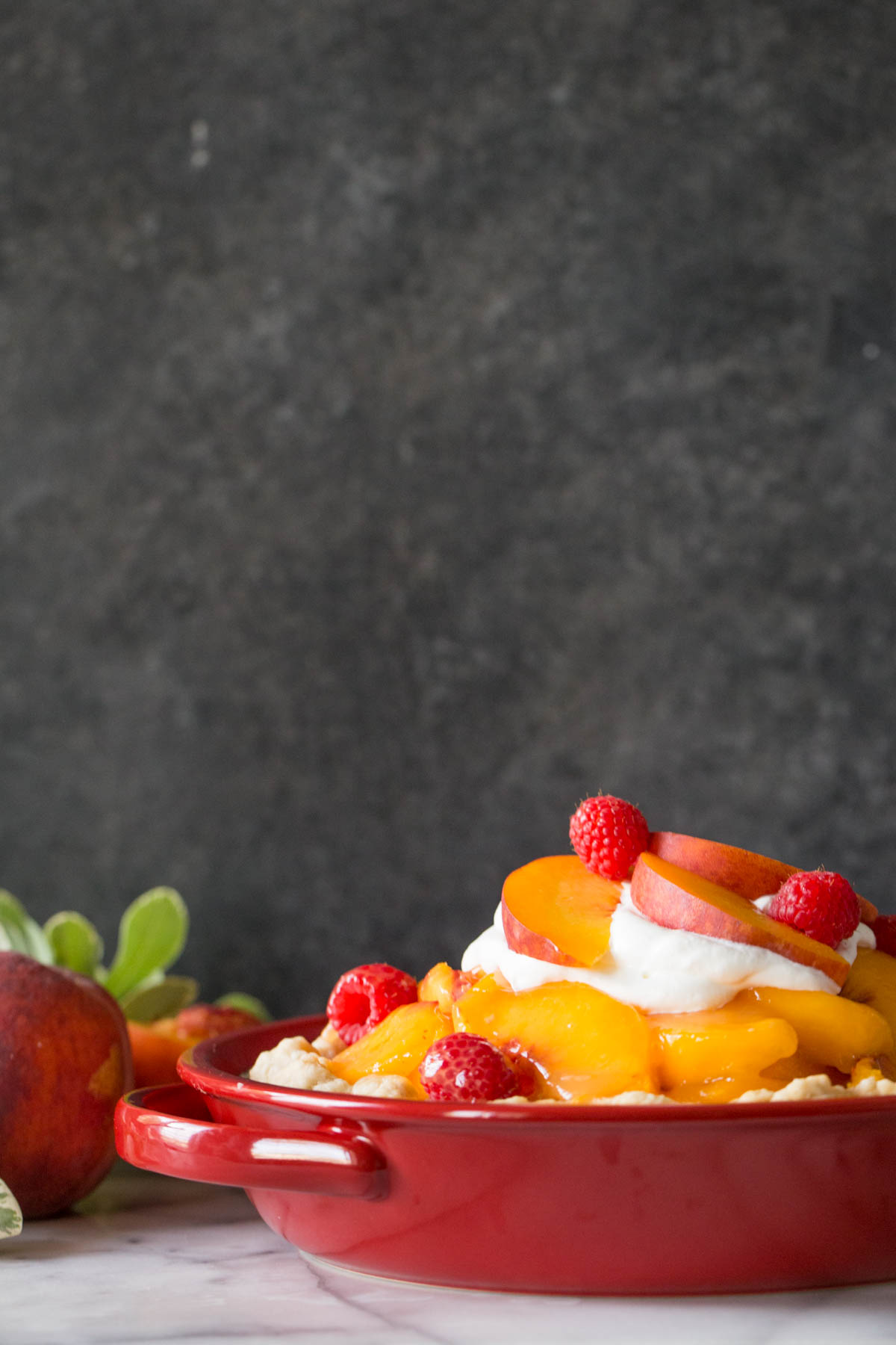 Fresh peach pie with homemade whipped cream in a red pie dish.