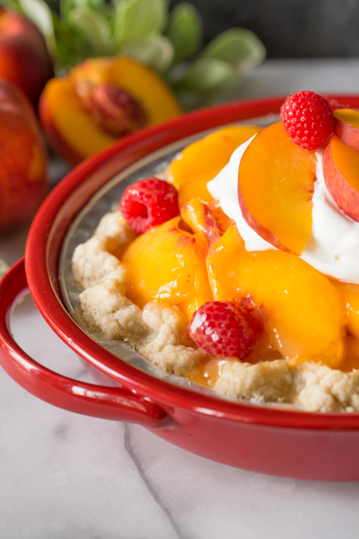 Fresh Peach Pie with whipped cream in a red pie dish.