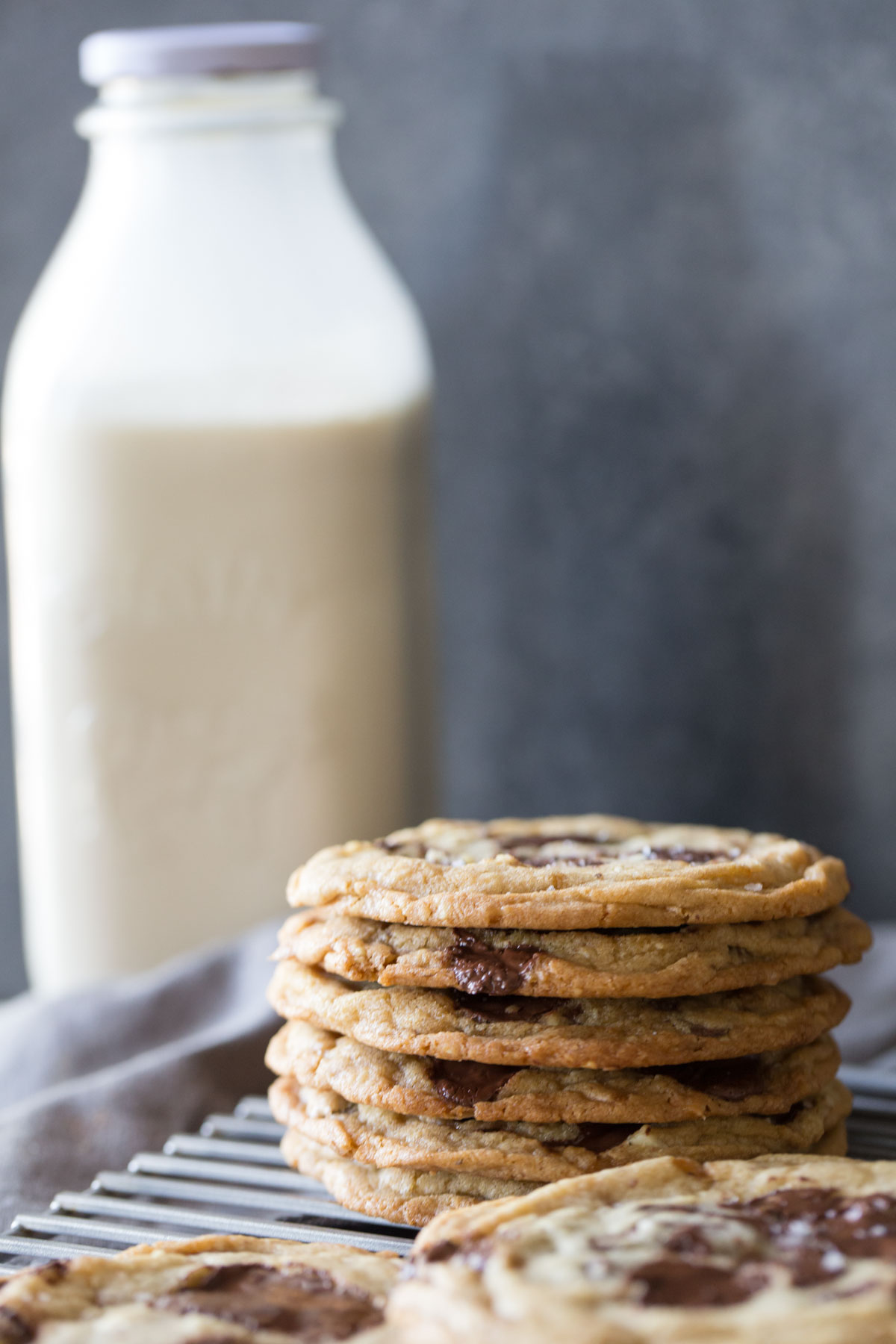 Toffee Almond Chocolate Chunk Cookies on a cooling rack with a bottle of milk in the background. 