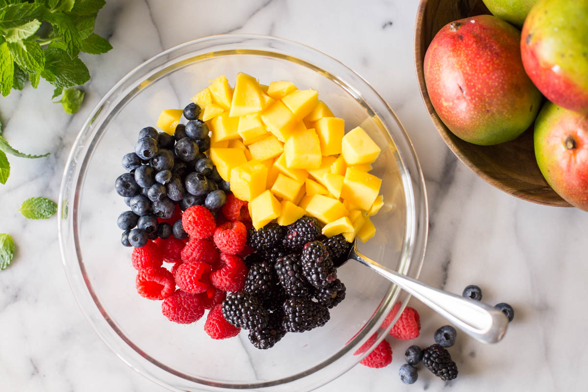 Fresh mango and berries in a glass bowl on a marble slab.