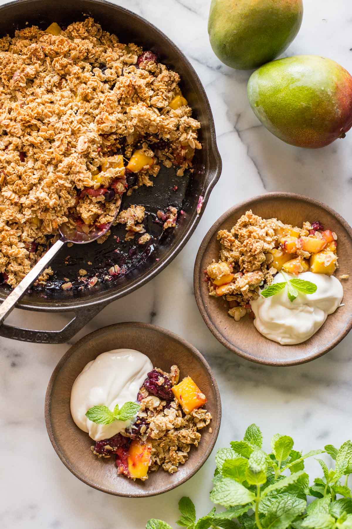 Mango Berry Breakfast Crisp in a cast iron skillet, with two bowls ready to serve.