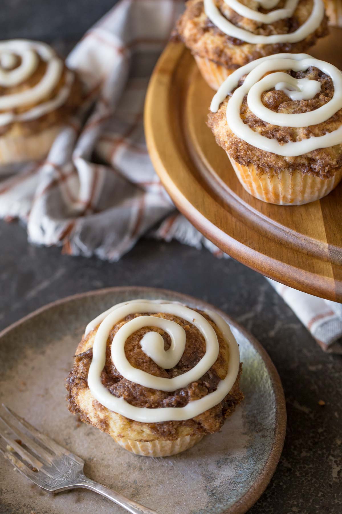 Cinnamon Roll Muffins with a cream cheese icing swirl on a wooden cake stand.