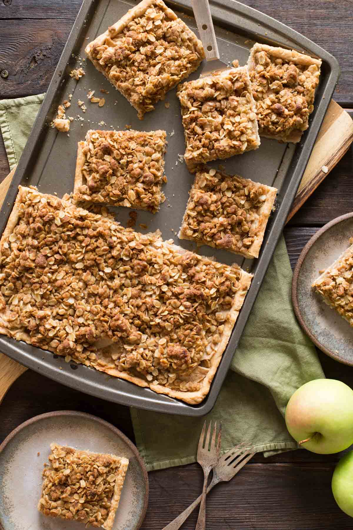 A top down view of a Dutch Apple Slab Pie with a few pieces cut out and fresh apples scattered around.
