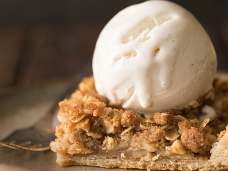 A close up view a piece of Dutch Apple Slab Pie with a scoop of vanilla ice cream on top.