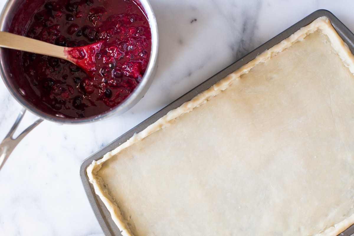 A jelly roll pan lined with dough and a sauce pan with triple berry filling in it.