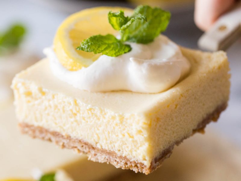 Close up view of the Best Creamy Lemon Bars on a marble slab topped with lemon slices, fresh mint and whipped cream.