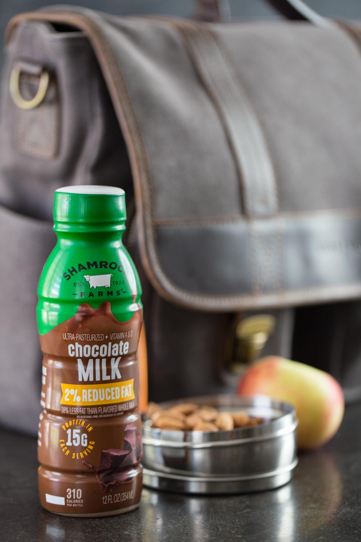 Chocolate milk with almonds and apple in front of a grey laptop bag.