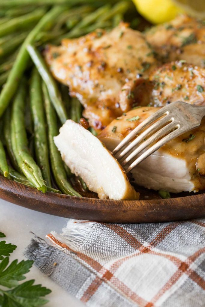 Close up shot of a slice of Best Ever Chicken Marinade with a fork and green beans in the background.