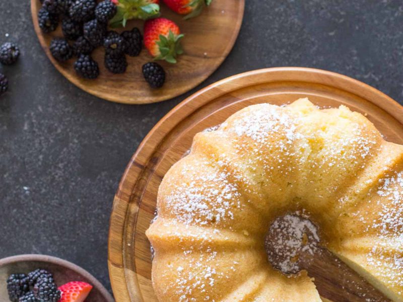 Kentucky Butter Cake on wooden cake stand with whipped cream and berries on a grey background.
